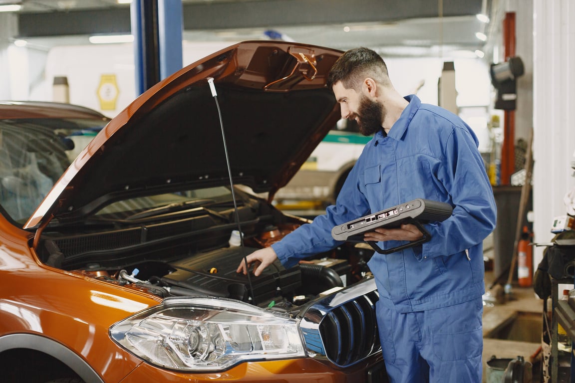 Man Wearing Blue Uniform Firxing Car while Holding Device